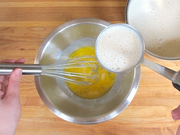 Tempering warm milk into beaten eggs.