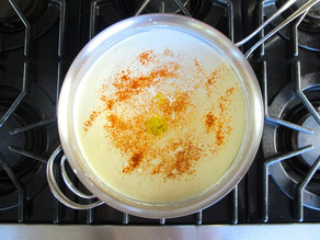 Whisking cheese and garlic into white sauce.