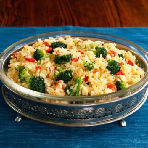 Delicious Zesty Broccoli Cheddar Rice served in a beautiful casserole dish, placed on top of a blue tablecloth