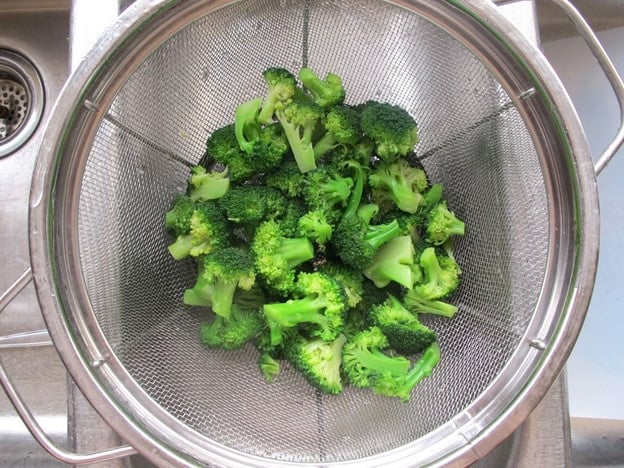 Draining cooked broccoli in a strainer.