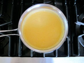 Whisking milk into a roux in a saucepan.