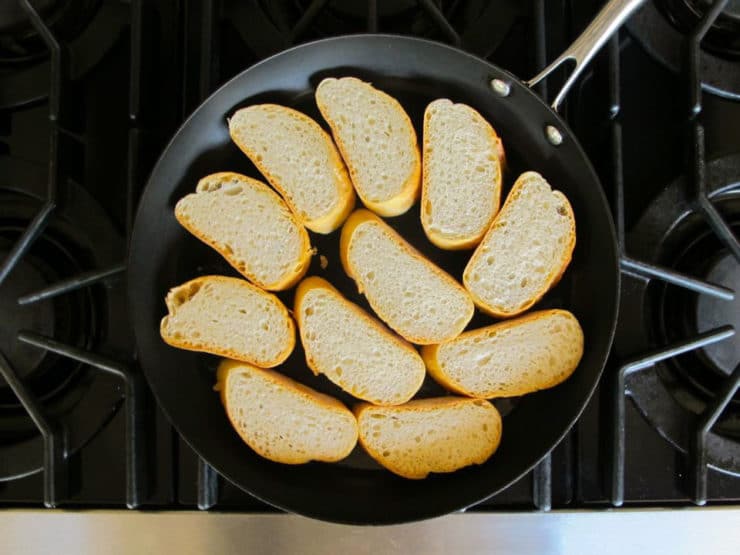 Toasting sliced baguette in a skillet.