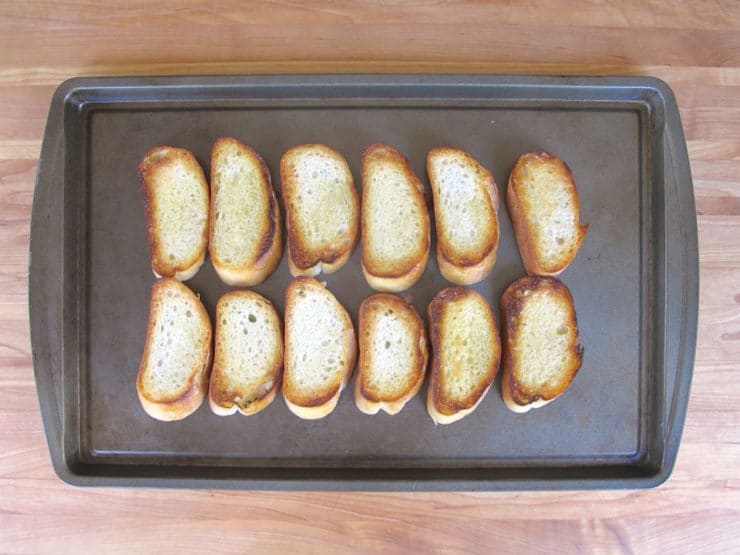 Sliced baguette on a baking sheet to keep warm in the oven.
