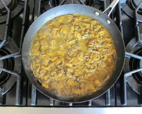 Vegetable broth added to sliced mushrooms in a skillet.
