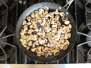 Sliced mushrooms sauteeing in a skillet.