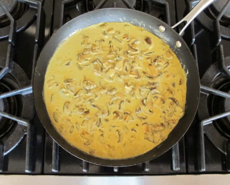 Cream added to sliced mushrooms in a skillet.