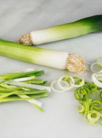 Horizontal shot - two leeks with julienne-cut and rings of leeks beside them on marble cutting board.