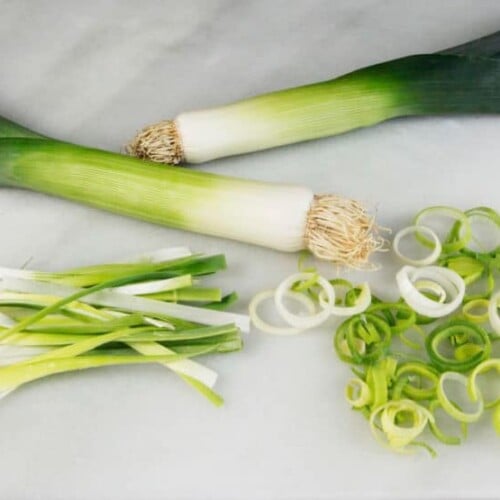 Horizontal shot - two leeks with julienne-cut and rings of leeks beside them on marble cutting board.
