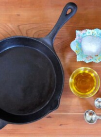 Clean seasoned cast iron pan on wooden background with oil, salt and measuring spoons on the side.