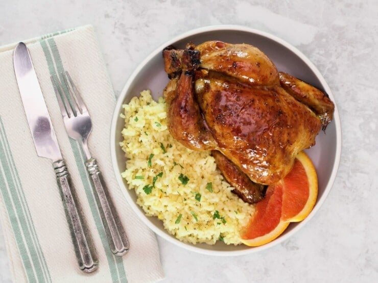 Overhead horizontal shot of a plate containing a citrus marinated game hen on a bed of rice, garnished with fresh orange slices.