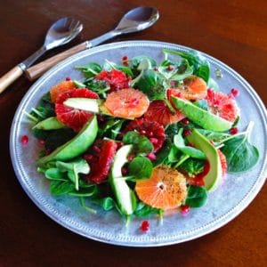 A vibrant citrus avocado salad with oranges, spinach, and pomegranate, drizzled with poppy seed dressing
