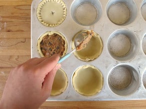 Adding meat filling to mini pie crusts.