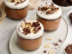 Horizontal shot of three glass dessert cups filled with a layered chocolate parfait.