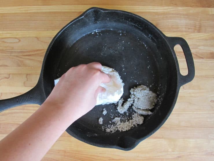 Hand cleaning salt and food particles from bottom of cast iron skillet.