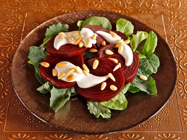 Roasted Beets with Tahini and Pine Nuts served over greens on a plate.