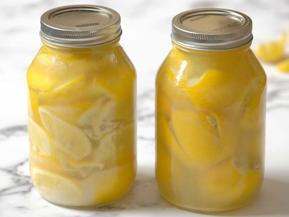 Two jars of preserved lemons on a countertop.