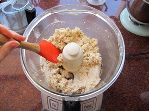 Scraping down the sides of a food processor with a rubber spatula.