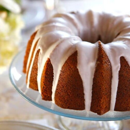 A Lemon Poppyseed Bundt Cake with a luscious icing drizzled on top, displayed on a glass plate