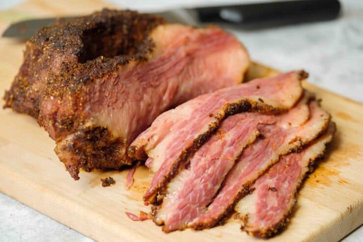 Close up horizontal shot - sliced pieces of brisket on a wooden cutting board with a chef\'s knife laying next to the board