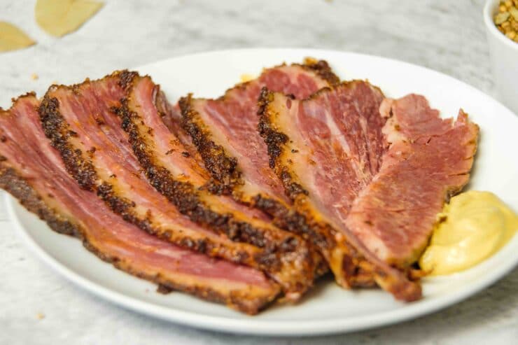 Horizontal shot - slices of brisket and a dollop of yellow mustard on an oval shaped white plate.