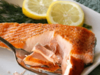 A seared salmon fillet on a white plate with lemon slices
