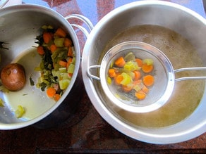 Straining vegetables out of chicken stock.