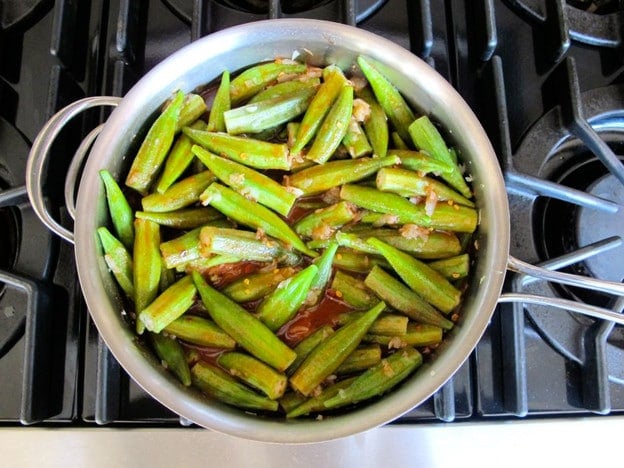 Pouring tomato sauce over cooked okra.