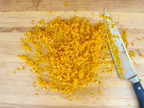 Mincing orange zest on a cutting board.