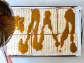 Pouring toffee mixture over matzo crackers on a baking sheet.