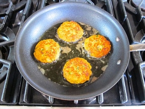 Salmon cakes frying in a skillet.