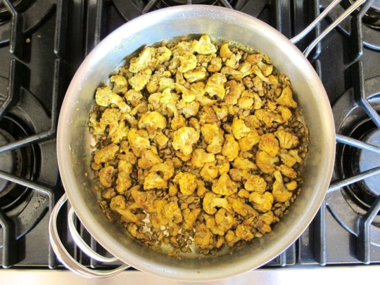 Cooked lentils added to cauliflower in a skillet.