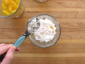 Adding coconut over oranges in a parfait cup.