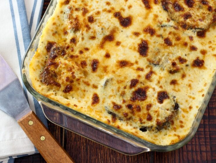 Overhead shot of Roasted Vegetable Moussaka in casserole dish on wooden tabletop.