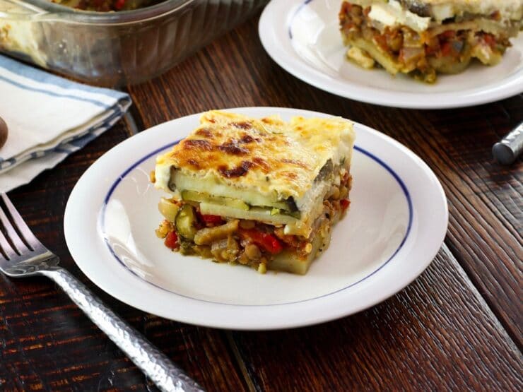 Close up of slice of Roasted Vegetable Moussaka on a small plate on wood table.