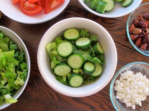 Adding sliced cucumbers to a quinoa bowl.