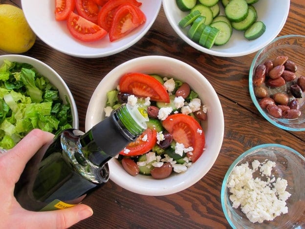 Drizzling olive oil over completed salad.
