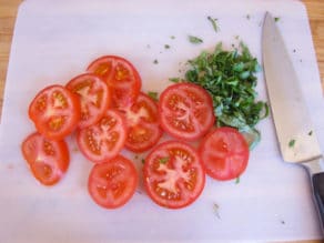 Sliced tomatoes and chiffonade of basil on a cutting board.