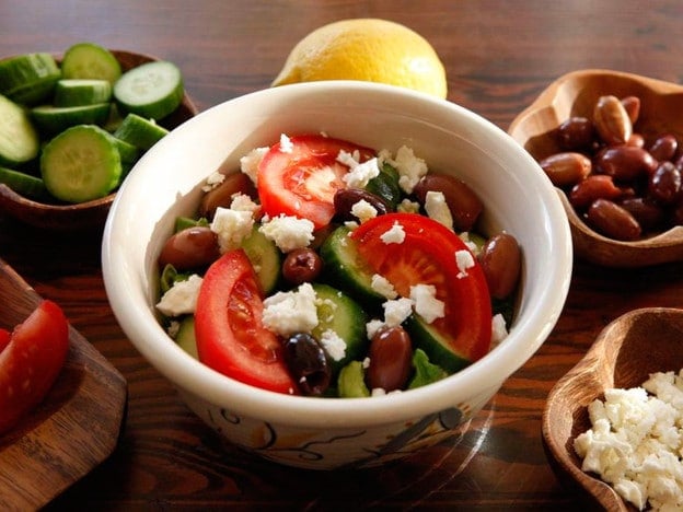 Greek Salad Quinoa Bowl with of chopped tomatoes, beans, quinoas, a lemon, and cheese in the back