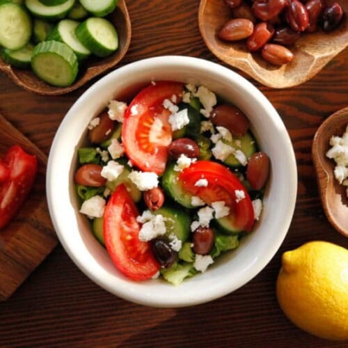 Greek Salad Quinoa Bowl with of chopped tomatoes, beans, quinoas, a lemon, and cheese in the back