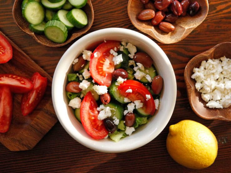 Greek Salad Quinoa Bowl with of chopped tomatoes, beans, quinoas, a lemon, and cheese in the back