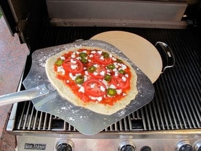Transferring pizza to preheated stone on grill.