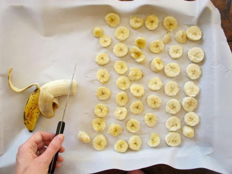 Sliced bananas on a parchment-lined baking sheet.
