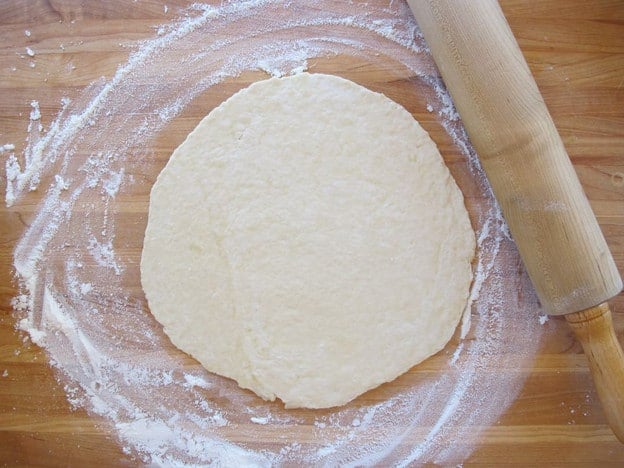 Pizza dough rolled out on a cutting board.