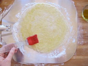 Brushing pizza dough with olive oil.