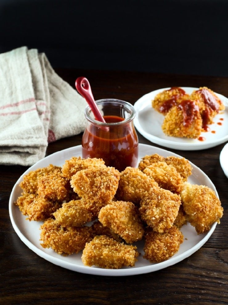 Smoky chicken schnitzel bites on plate, vertical shot, wooden table, nuggets with sauce in background.