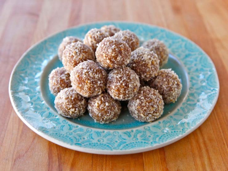 Aqua-colored plate of date truffles rolled in coconut on a wooden cutting board background.