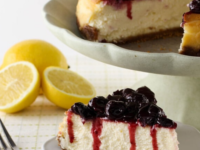 A slice of creamy New York Cheesecake with a golden crust, topped with a fresh blueberries
