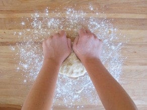 Kneading pizza dough on a cutting board.