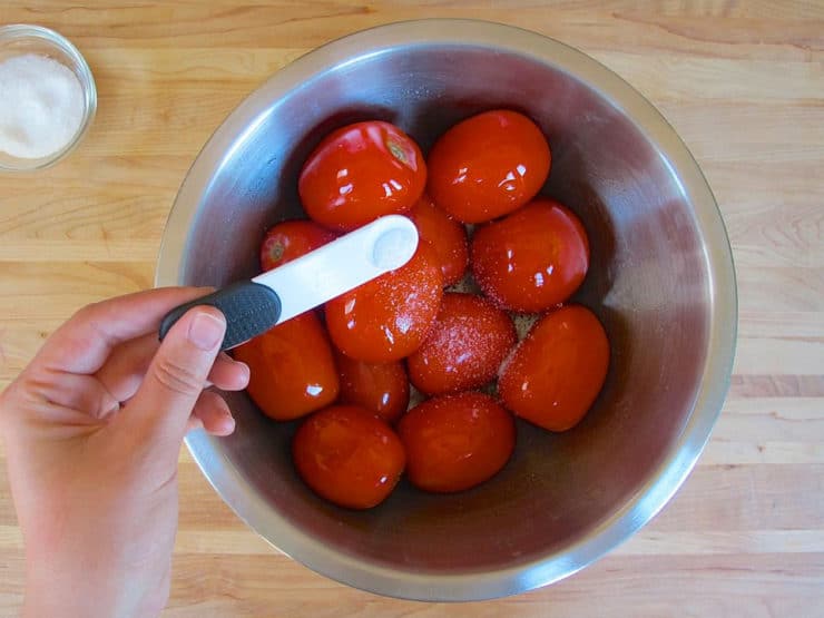 Adding oil and salt to Roma tomatoes in a bowl.