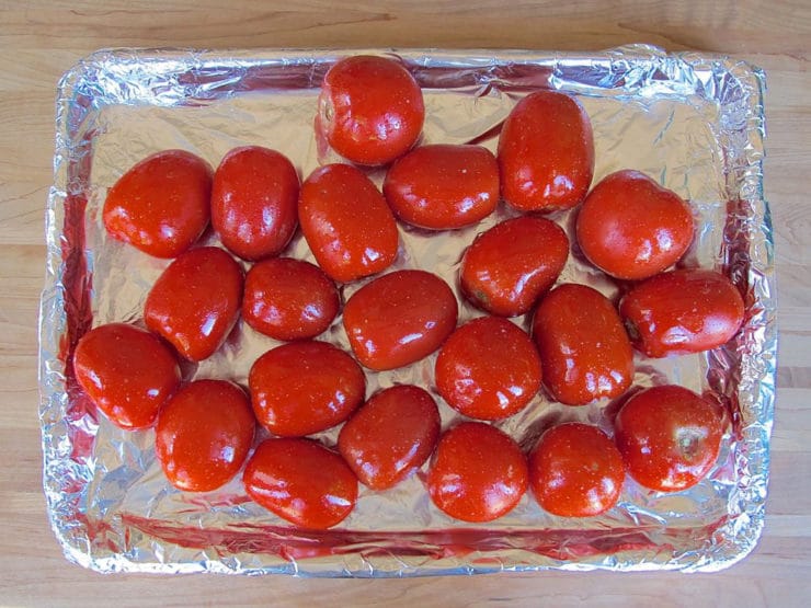 Oiled tomatoes on a lined baking sheet.
